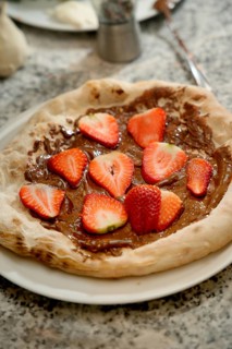 A freshly made dessert pizza topped with rich chocolate spread and sliced strawberries, served on a
