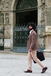 Side view of a mixed-race insurance salesman with afro hair walks confidently outside a historic,