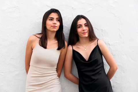 Young sisters in fashionable dresses, one in black and the other in white, stand against a textured