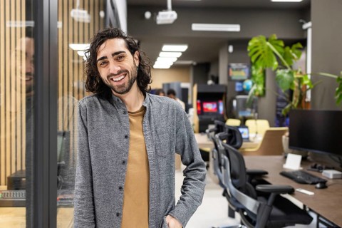 A man smiling in a contemporary office setting, surrounded by modern furniture and plants. The