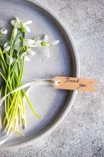 Top view of fresh spring snowdrops neatly arranged in a textured grey tray, accompanied by a