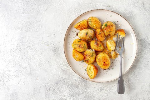 Half-eaten fried new potatoes, with butter and dill, on a white plate, with a fork, at home, no