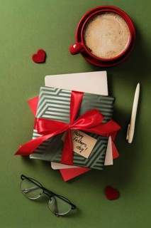 Father's Day flat lay: gift box, red coffee cup, eyeglasses, pen, envelopes, and hearts on a green