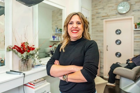 Confident woman hairdresser standing with crossed arms, smiling at the camera inside her brightly