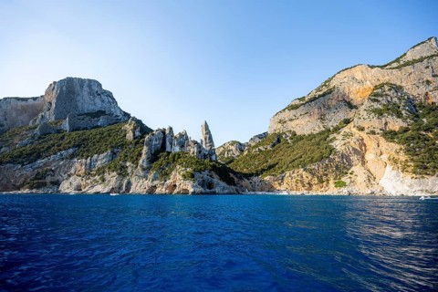 Picturesque rocky coast, cliffs with caves in the morning light, L'Aguglia rock peak, blue sea and