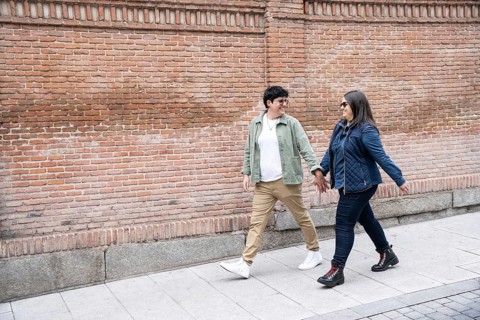 A joyful lesbian couple walks hand in hand along a brick wall, enjoying a casual day. Their