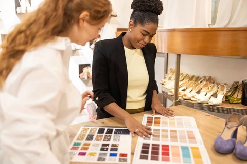 Two women engaged in a color selection task in a fashion boutique, surrounded by shoes. They review