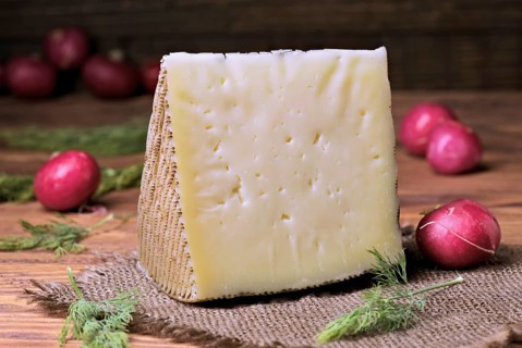 A wedge of cheese sits on a burlap cloth with fresh radishes scattered around. The rustic wooden