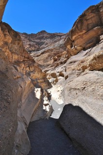 Sunny narrow passage of a hiking trail between high rock walls under blue sky, Death Valley