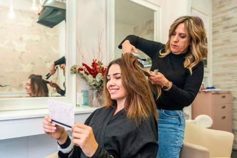 Professional hairstylist straightening client's long brown hair in a modern beauty salon, focusing