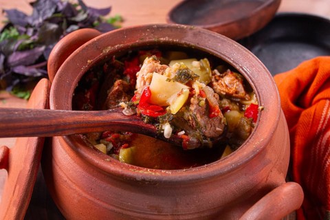 Chanakhi, a Georgian dish. in a clay pot, on a wooden table, stewed meat with vegetables, homemade,