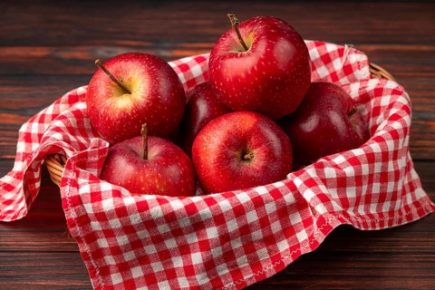 Basket with fresh, red apples on checkered cloth on a dark wooden background