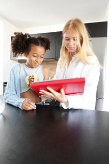 A young woman and a girl stand in a modern kitchen, smiling and enjoying time together. The woman