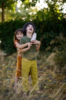 Two children playing outside on a sunny day. One child wearing a hat holds a plush toy while the