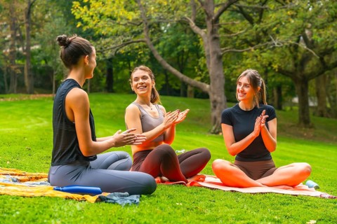 Women friends sitting on yoga mats, clapping hands and smiling happily, sharing a moment of
