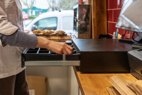 Baker or shop assistant in an apron opening the cash register drawer, preparing to handle money