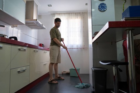 A man is seen mopping the floor in a modern kitchen, reflecting a typical household chore. He is