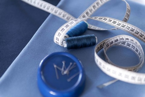 A close-up view of sewing tools including a white measuring tape, two blue thread spools, and a pin