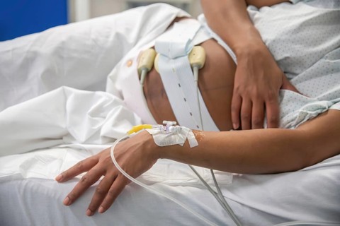 Cropped unrecognizable woman resting in a hospital bed, prepared for childbirth with medical