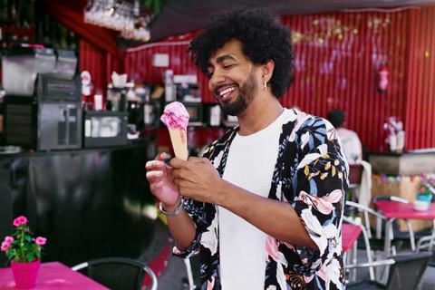 A cheerful man enjoying a colorful ice cream cone at an outdoor cafe during a warm summer day,