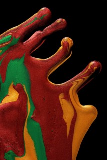 Vibrant metallic paints in red, green, and gold hues dramatically drip and blend on a dark