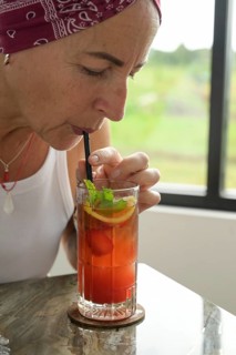 A mature woman with a red headscarf is pictured sipping a colorful Es Teh Nusantara tea drink