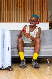 LGBTQIA+ man with vibrant blue hair and headphones sitting on a couch, browsing a smartphone next