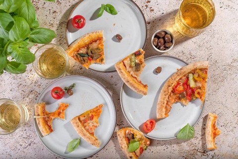 Top view of rustic vegetarian pizza slices with zucchini, eggplant, bell peppers, and basil.