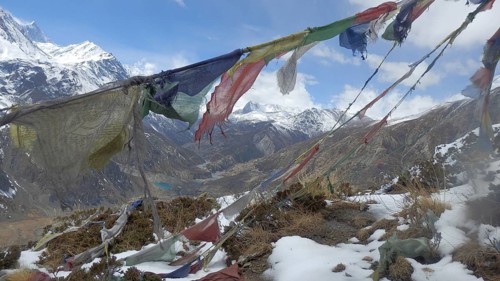 Colourful prayer flags overlook a snowy valley in the high mountains, trekking at Annapurna