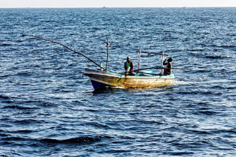 Two people in a wooden fishing boat sail across the vast sea, the fishing boats near Matara in the