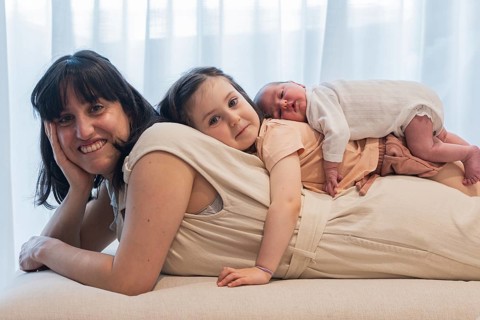 Young family enjoying a tender moment as the big sister lovingly lies beside a newborn baby. The