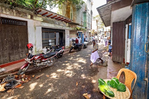 Narrow street with leaves on the ground, some motorized vehicles, local architecture in the