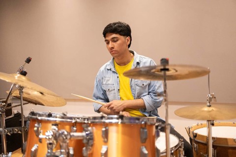 A drummer in a recording studio, deeply focused, playing drums. The space is equipped with