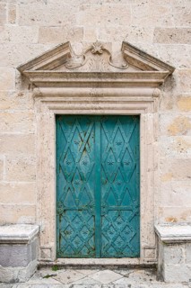 Antique green wooden door with elaborate decorations embedded in a stone wall, The island of Gospa