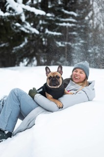 Woman enjoying a fun winter day with her dog, surrounded by snow-covered trees. Both dressed