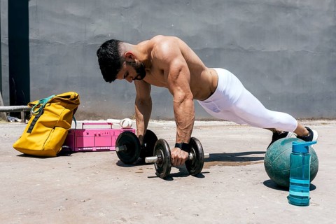 A physically fit man performs an intense outdoor workout using dumbbells and a medicine ball,