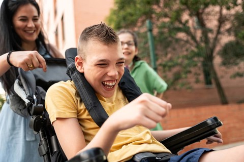 A mother joyfully spends time outdoors with her children, including a girl with a tracheostomy and