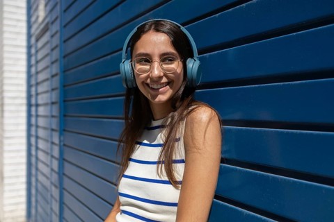 A woman enjoys her music while leaning against a modern blue wall in the city. She embodies a
