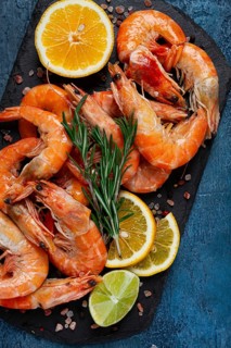 Freshly frozen shrimp, with lemon and rosemary, on black slate, close-up, top view, no people