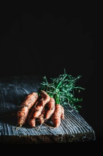 Organic carrots with vibrant greens rest on a textured wooden surface, emphasizing their fresh