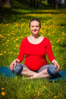 Pregnancy yoga exercise, pregnant woman doing asana Sukhasana easy yoga pose outdoors on grass lawn