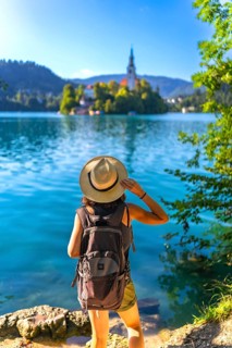 Female tourist wearing backpack and summer hat enjoying breathtaking view of lake bled island with