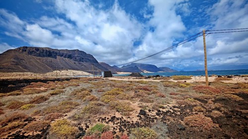 Wide landscape with dry, colorful vegetation, mountains and power poles under blue skies, Calhau,
