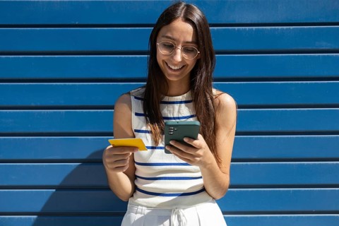 A woman enjoys outdoor city life, engaging with technology through her smartphone and credit card.