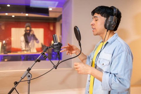 A musician records vocals in a modern studio, wearing headphones and performing passionately into a