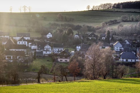 Partial view of Langenholdinghausen with village character amidst green hills in warm sunlight with