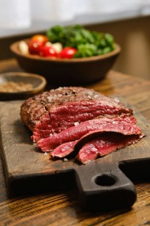 A cutting board holds slices of roasted steak. A bowl of fresh vegetables, including tomatoes and