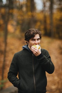 A man enjoys a fresh apple in a serene Quebec forest during autumn, surrounded by vibrant fall