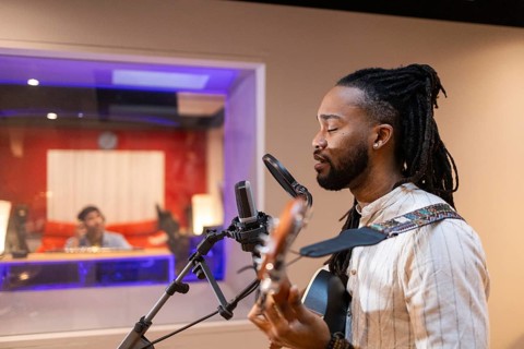 A musician passionately plays guitar and sings into a microphone in a professional recording studio