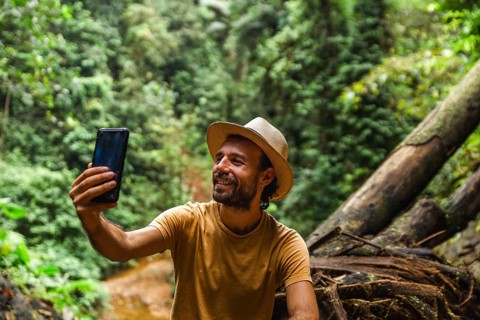 A young man smiling while taking a selfie with mobile phone in the Choco Andino rainforest in